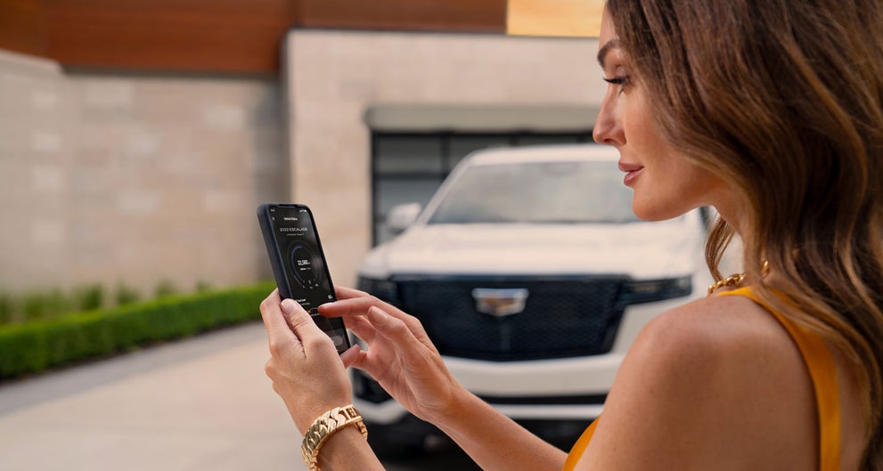 lady checking her mobile with a Cadillac vehicle background | Tom Clark Cadillac in Denton TX